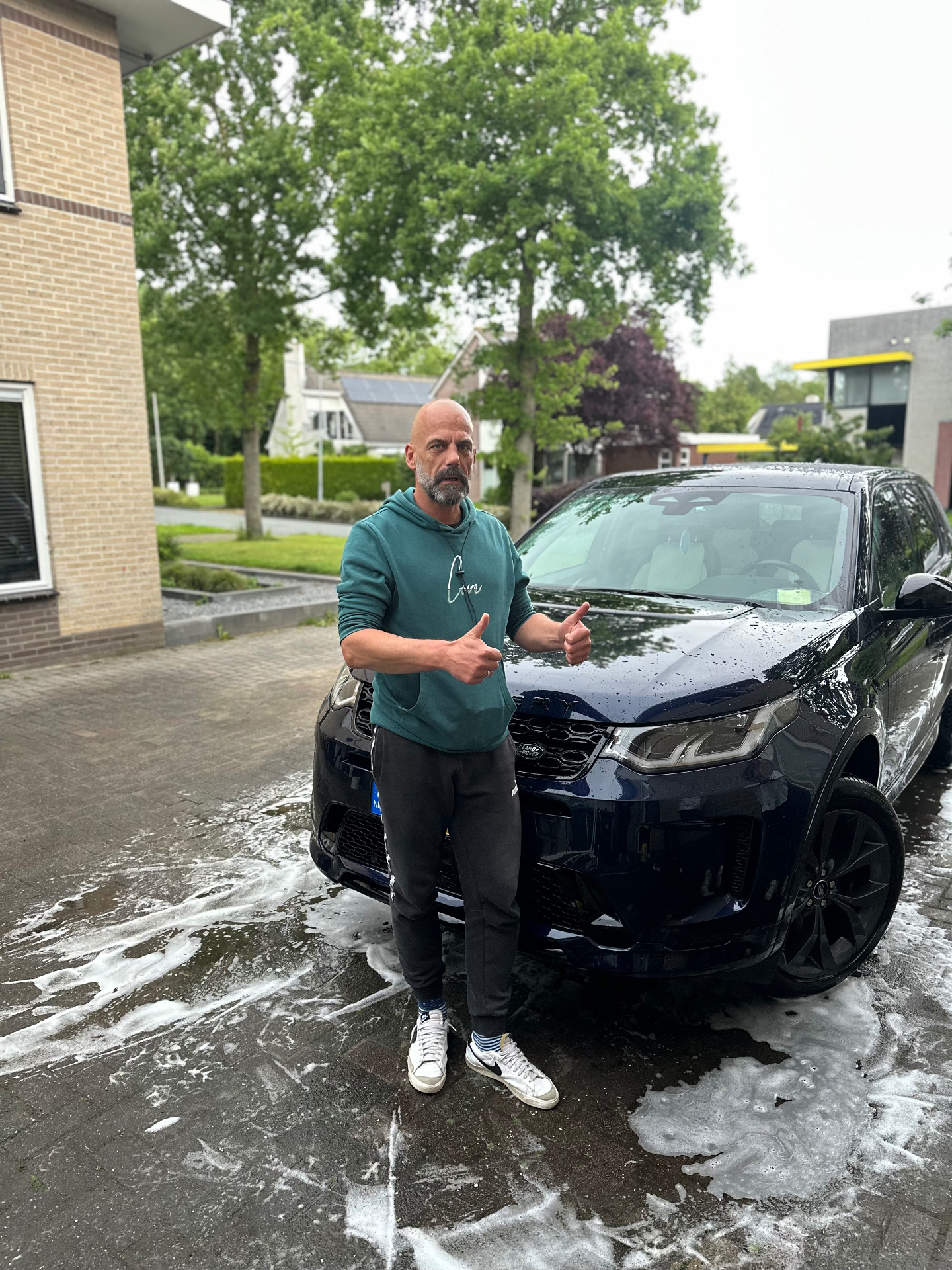 Tevreden klant naast een donkere Range Rover na een wasbeurt